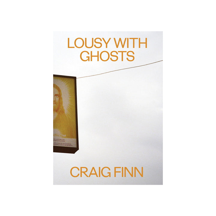 The book cover for Lousy With Ghosts from Craig Finn features a partial religious icon on a sign set against a cloudy sky, with the title and author’s name in bold orange text.
