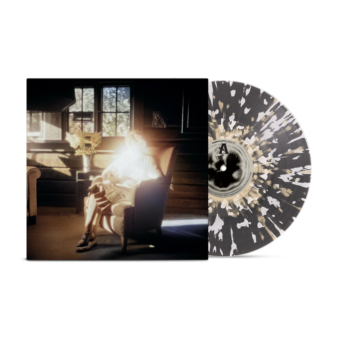 A Limited Edition Common Sage Vinyl with a black, white, and beige splatter design sits next to its album cover of a glowing figure in an armchair. Available November 22, 2024.