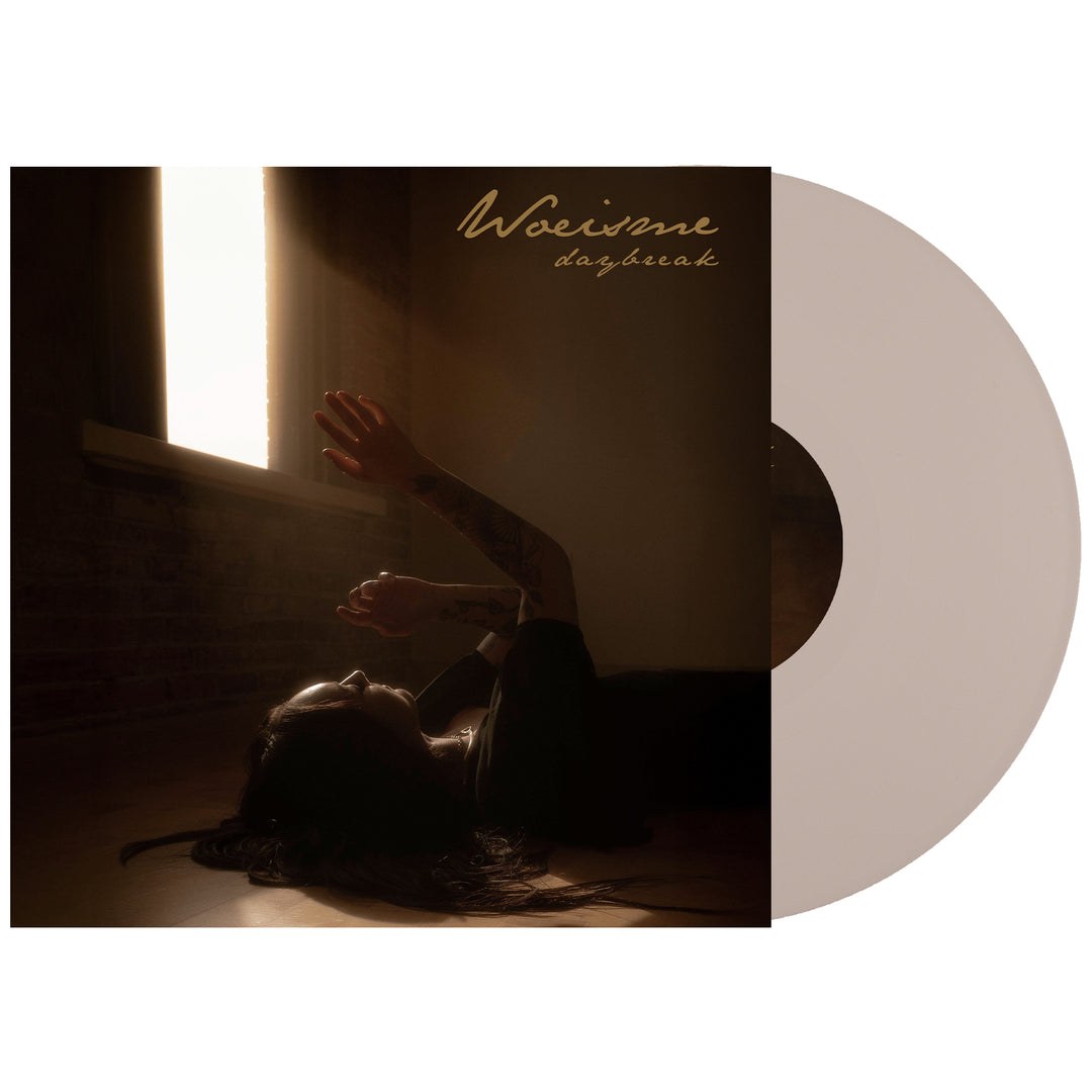 A Woe Is Me Daybreak Bone Vinyl LP partially slides out from its cover, showing a person in warm window light with raised arms. The album title appears at the top. Includes full album digital download with presale.