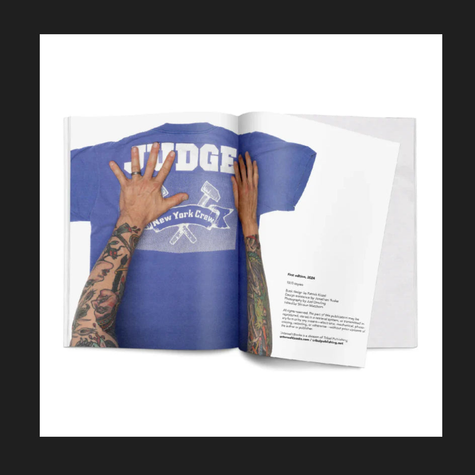 An open magazine from Unterwelt Books shows tattooed arms holding a blue Merchnow American hardcore T-shirt with JUDGE and New York Crew above crossed hammers, part of the Ryan Bannahan collection. The right page is covered in text.