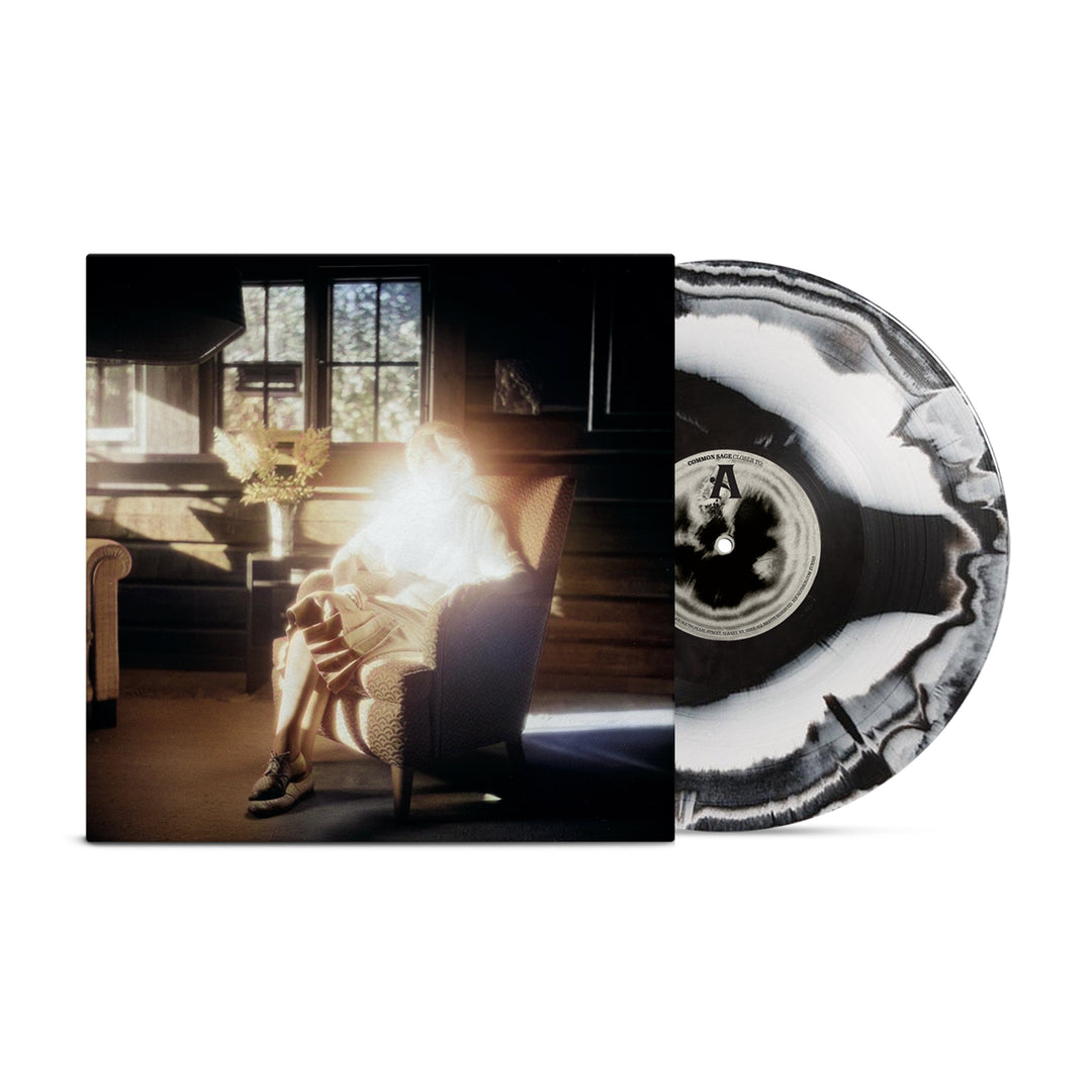 A black-and-white marbled limited edition vinyl by Common Sage is partially visible behind its cover, which features a person in a sunlit armchair in a wooden room with their face obscured by light.