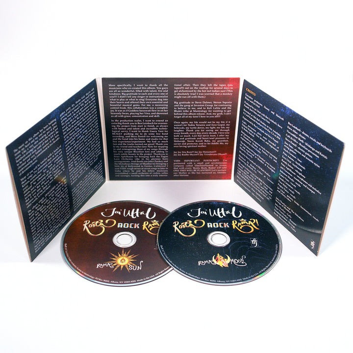 Two Jai Uttal CDs—one with a sun design labeled “Ramblin’ Sun,” the other with a moon and “Ramblin’ Moon”—stand upright beside an open booklet featuring R.A.S.A. lyrics, info, and rock-inspired artwork.
