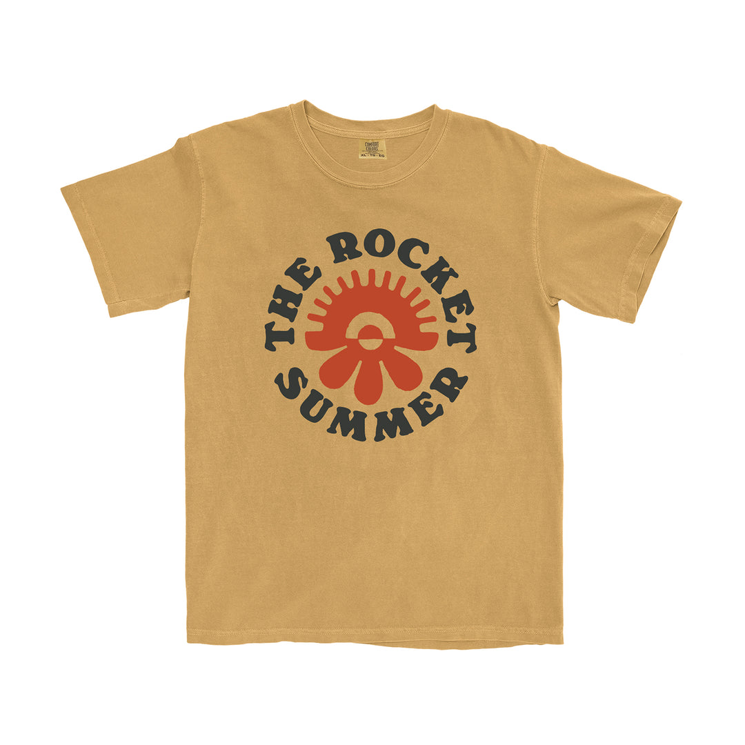 This tan Comfort Colors tee by The Rocket Summer features bold black “THE ROCKET SUMMER” text encircling a red sunburst/flower graphic on the chest. Garment-dyed for softness and a relaxed fit for comfort.