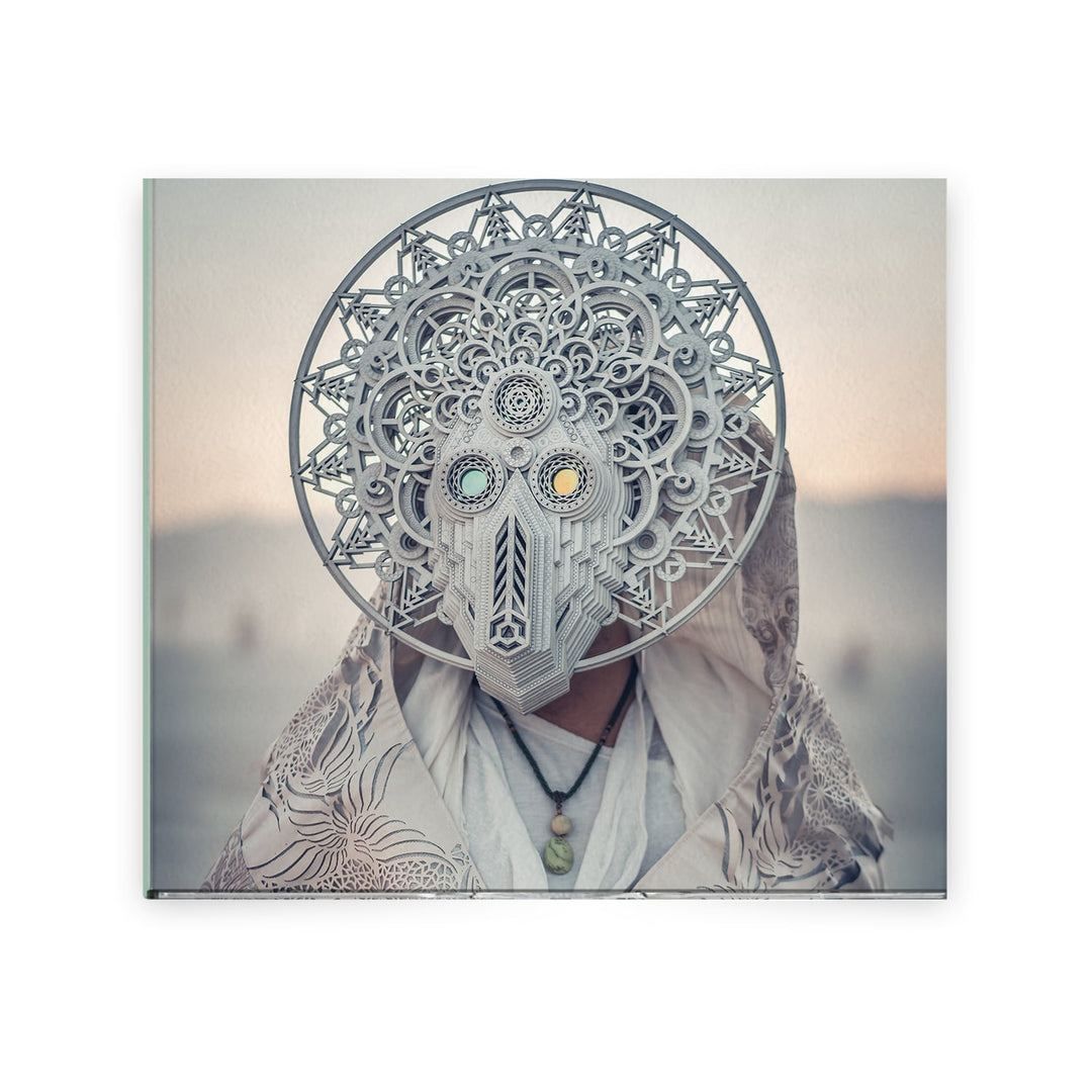 A person in an intricate geometric mask with mandala-like circular patterns and a patterned cloak by Eidola stands like an architect of music, set against a softly blurred background in neutral tones.