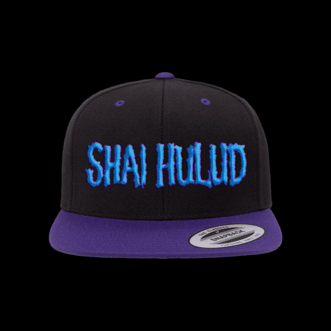 A black Shai Hulud snapback hat features a purple brim and blue embroidered SHAI HULUD text on the front, displayed against a plain black background.