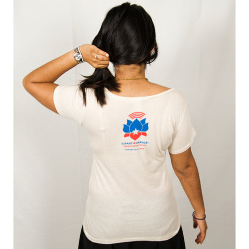 A person with long dark hair, facing away, wears a Mantralogy organic cotton white t-shirt featuring a blue and red lotus with Chant4Change text on the back. They hold up their hair and wear a bracelet against a plain white background.
