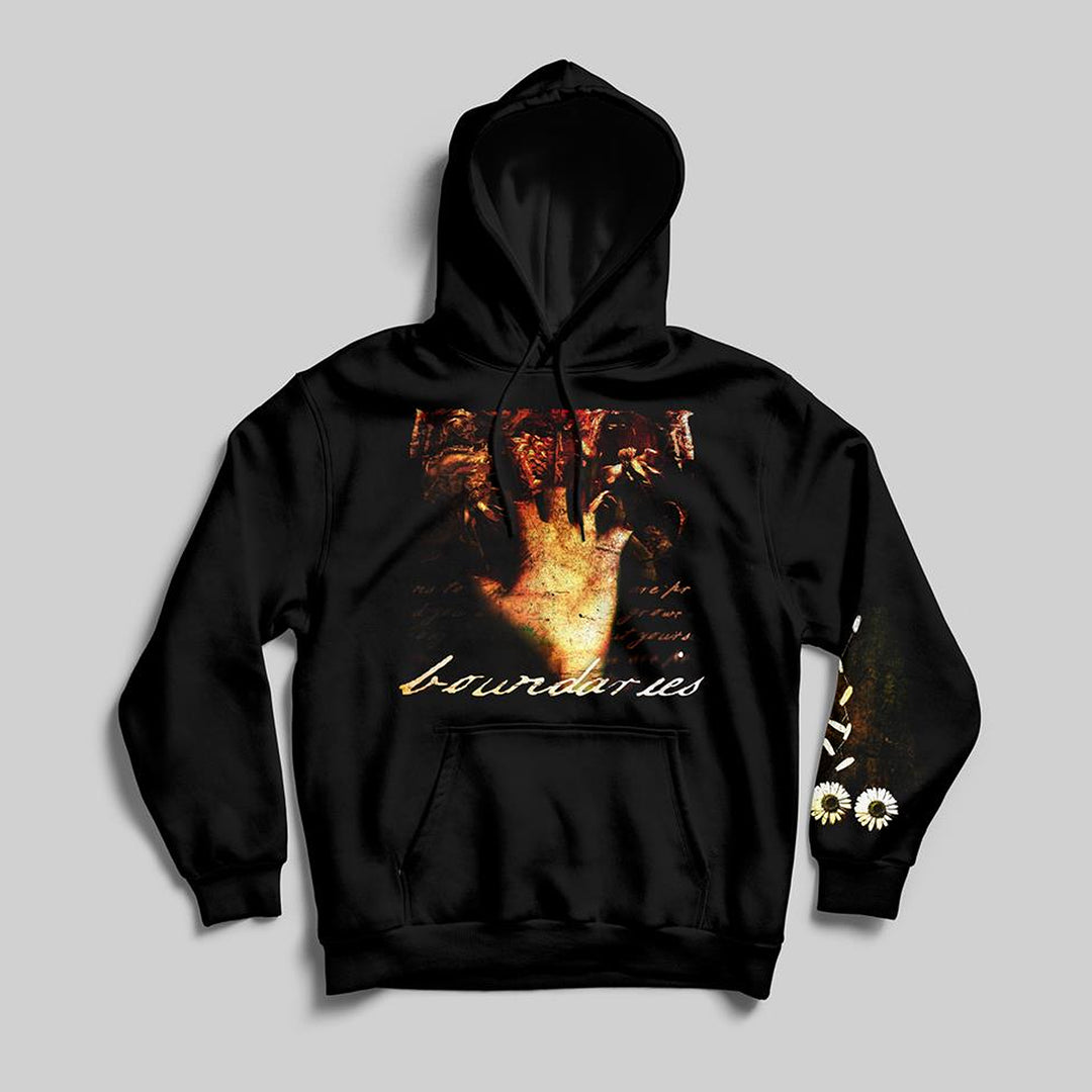 The Boundaries classic fit pullover hoodie features a raised hand graphic over a dark background with “boundaries” in script, soft ring-spun cotton, and white daisy details on the left sleeve near the wrist.
