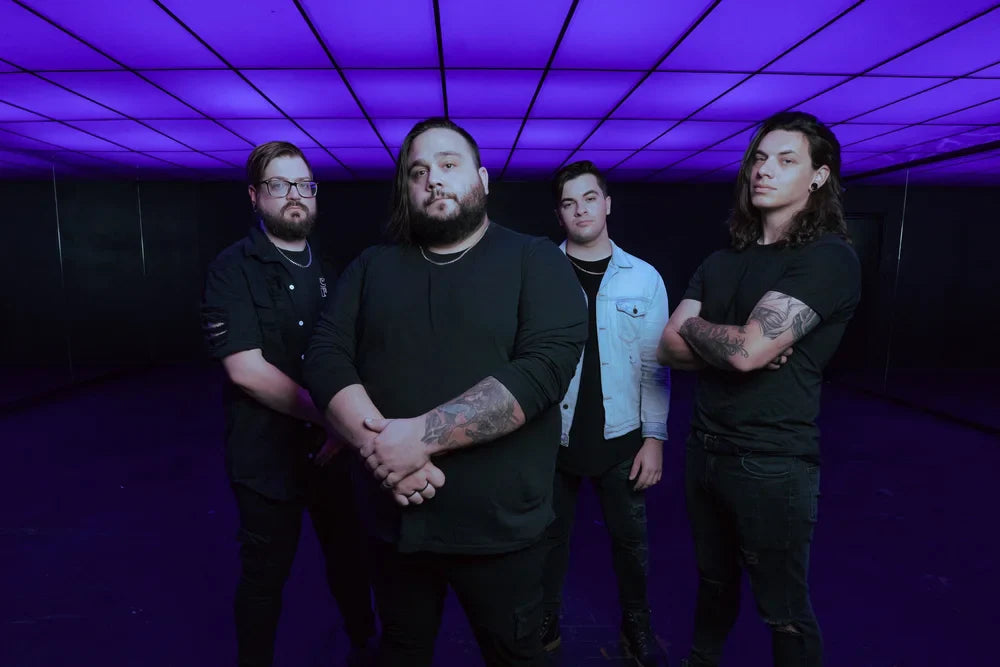 Four men stand side by side under a glowing purple ceiling, facing the camera with serious expressions. They wear dark clothing, and two have visible tattoos on their arms.