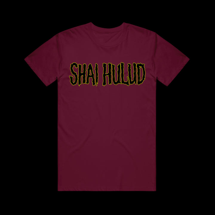 A maroon Shai Hulud Comfort Colors t-shirt with bold, jagged yellow SHAI HULUD lettering outlined in black across the chest, displayed against a plain black background.
