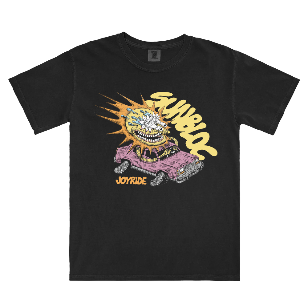 Black Sunbloc Comfort Colors shirt with a grinning cartoon face bursting from a purple car with orange flames. "Sayuloc" and "Joyride" are boldly printed above and below in stylized text.
