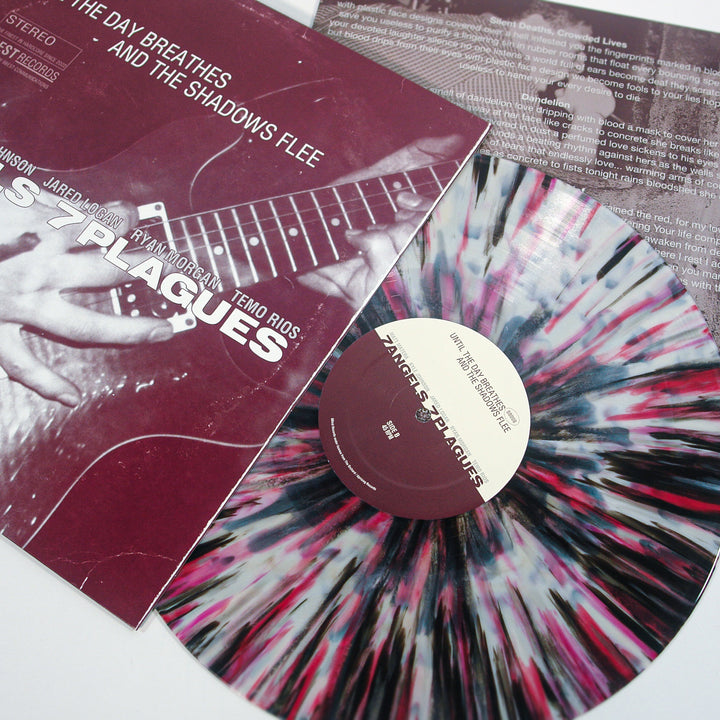A maroon, white, and black splatter-patterned vinyl record by 7 Angels 7 Plagues titled "The Day Breathes and the Shadows Flee" rests partially in its album sleeve, with photo and title text visible.