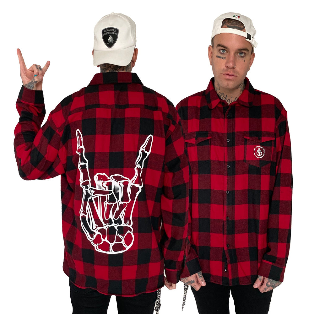 A man models Stay Sick Clothing’s flannel, shown from front and back. The shirt features a large skeleton hand flashing metal horns on the back. He wears a white cap, has tattoos, and keeps a neutral expression—ideal for fall/winter.