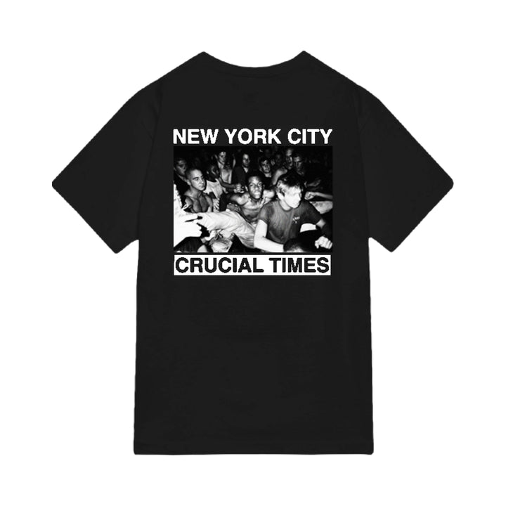 The Crucial Times black Comfort Colors tee features a black-and-white crowd photo with bold white "NEW YORK CITY" above and "CRUCIAL TIMES" below. Available now for presale; ships 5/15/26.