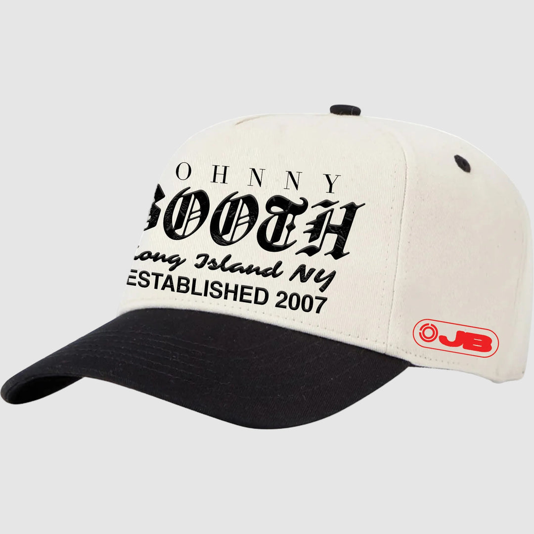 A black Johnny Booth snapback hat with white and black panels, black "Johnny Booth, Long Island NY, Est 2007" text on the front, and a red JB logo on the side.