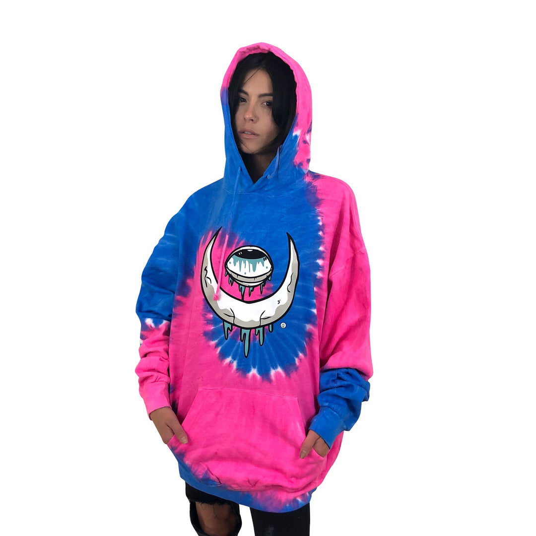 A person wears a Stay Sick Clothing Flo Blu pink and blue tie-dye hoodie featuring a large dripping eye moon graphic in the center, standing against a white background.