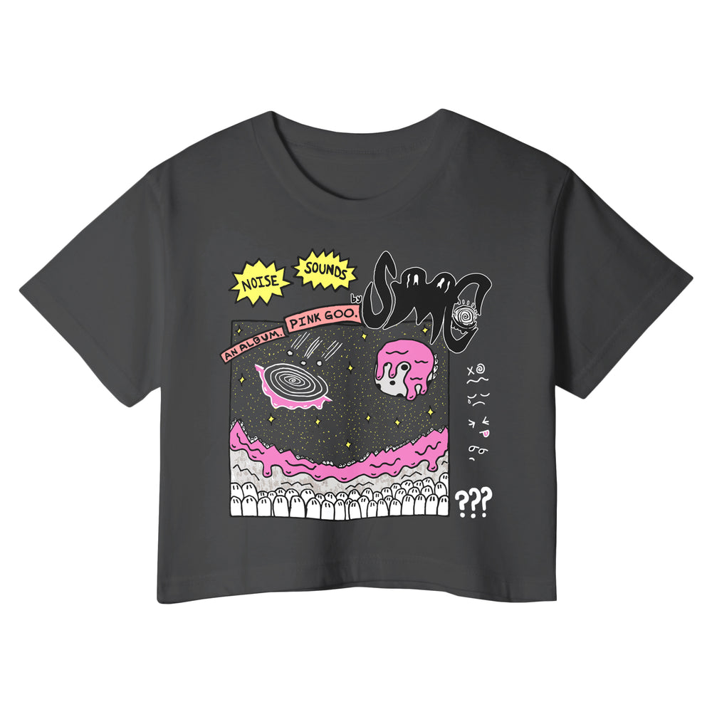 A black crop T-shirt by Strawberry Milk Cult features a colorful cartoon graphic with planets, stars, pink goo, and comic-style text reading NOISE SOUNDS, PINK GOO, ??? plus playful abstract doodles.
