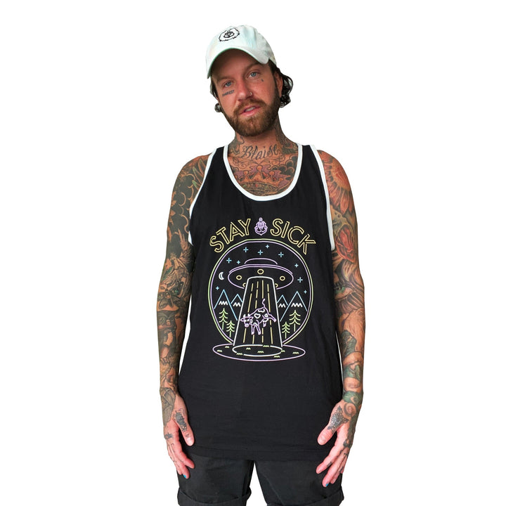 A bearded, tattooed person wears a white cap and a black Stay Sick Clothing tank top with a neon abduction graphic and the words STAY SICK, standing against a white background—a bold nod to Neon Fashion.