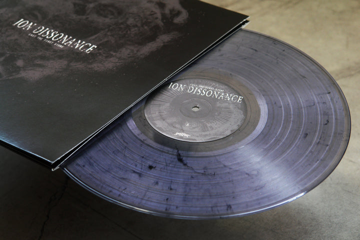 A translucent gray Salt & Pepper vinyl with black marbling partially slides out of its matching Ion Dissonance-branded album cover, resting on a smooth gray surface.