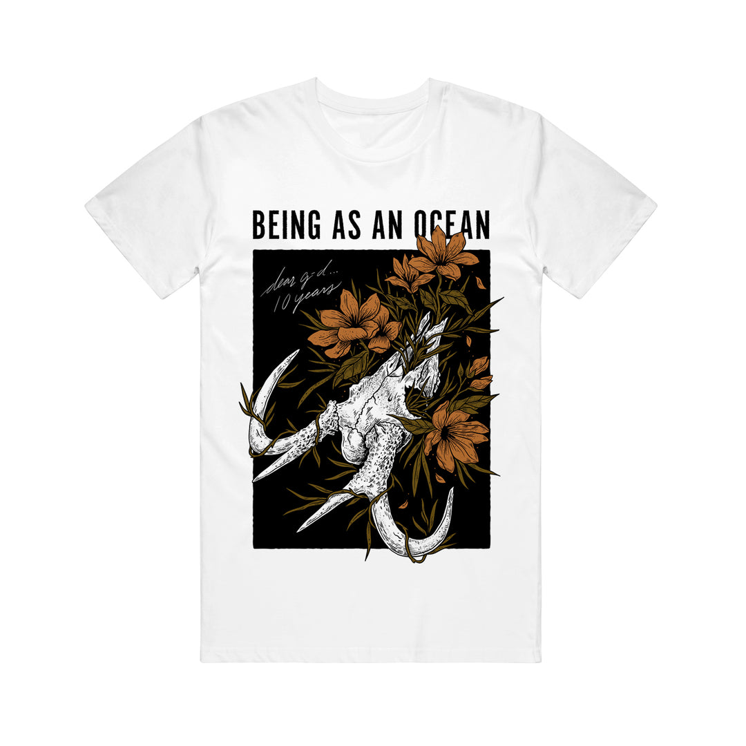 image of a white tee shirt on a white background. the tee has a full body print that says on the top in black being as an ocean with the image of a deer skull below with orange flowers surrounding it.