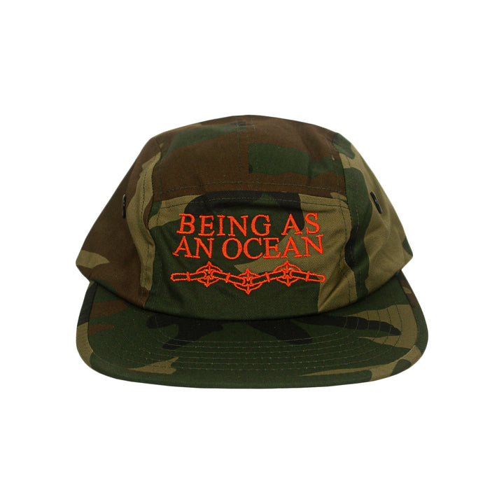 Camo five-panel cap with BEING AS AN OCEAN and a barbed wire graphic embroidered in orange on the front.