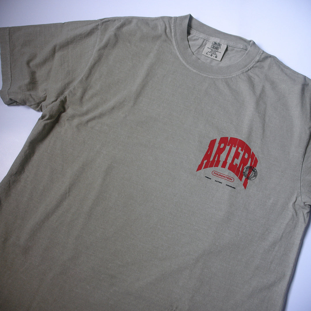 A light gray, garment-dyed Artery Foundation T-shirt with "ARTERY" in bold red and small black graphics and text printed below it on the left chest.