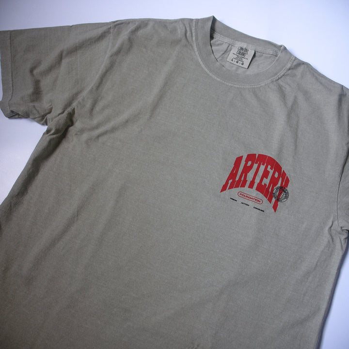 A light gray, garment-dyed Artery Foundation T-shirt with "ARTERY" in bold red and small black graphics and text printed below it on the left chest.