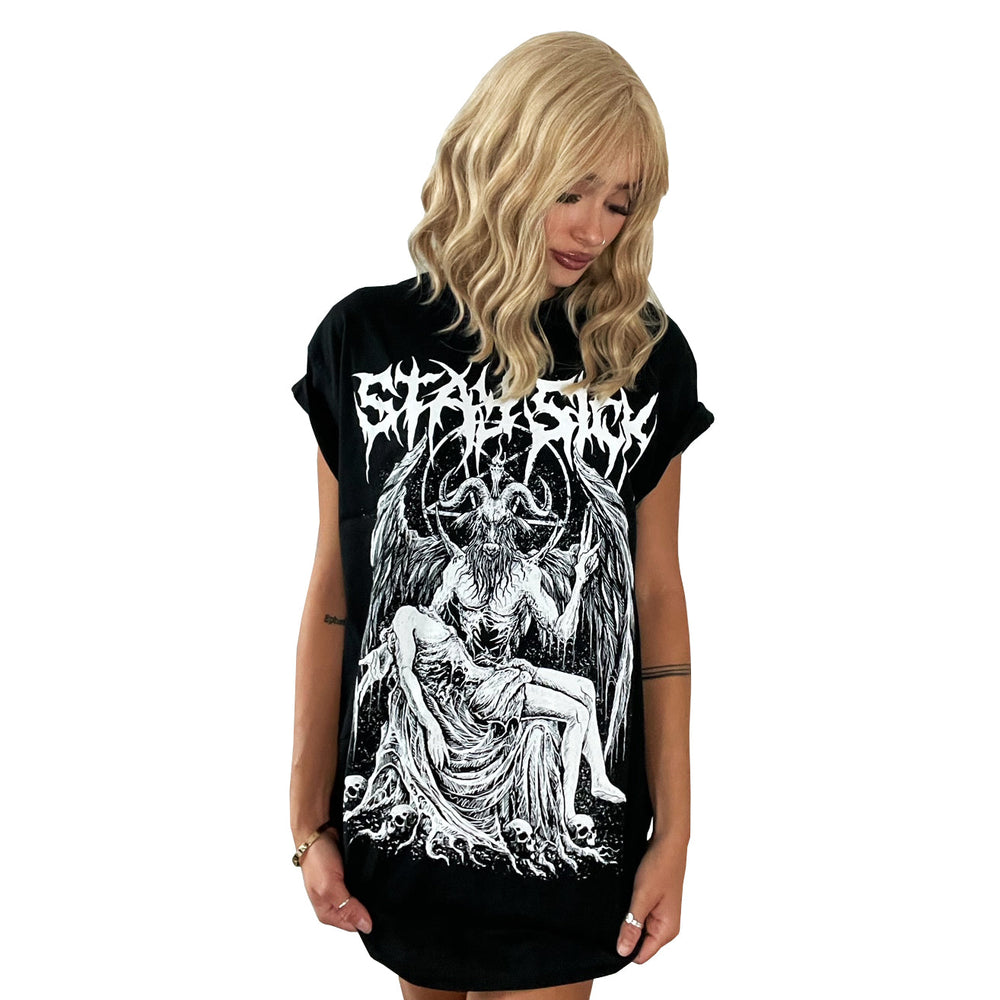 A person with wavy blonde hair looks down, wearing a loose Stay Sick Clothing Baphomet T-Shirt featuring a detailed white graphic of the dark, mythical winged creature and a seated figure on a plain white background.