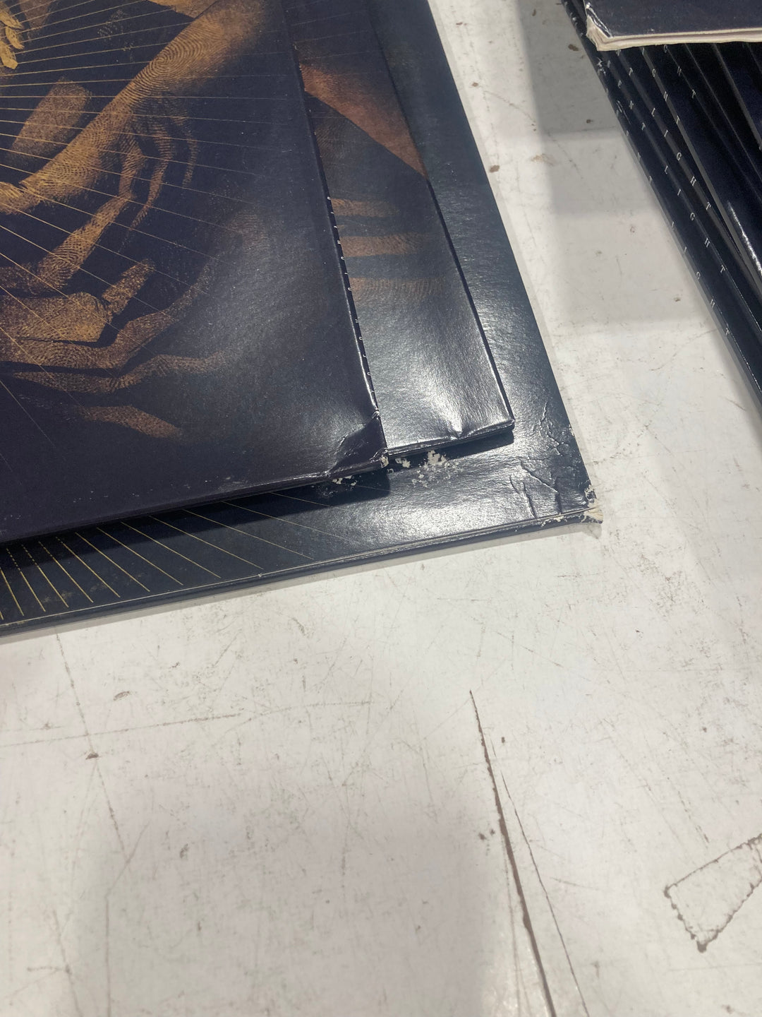 Close-up of two dark-colored Misery Signals vinyl covers with gold designs and worn corners on a scratched white surface. The visible wear adds character, while the tracklist hints at the music inside.