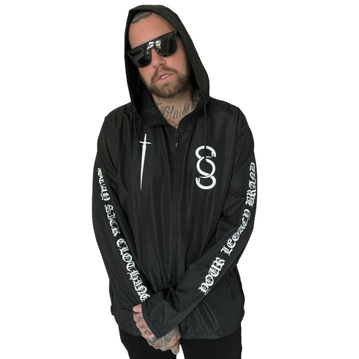 A man with sunglasses and visible neck and hand tattoos stands with arms crossed, wearing a black Stay Sick Clothing zip-up jacket featuring white graphics and text on the sleeves. The background is plain white.