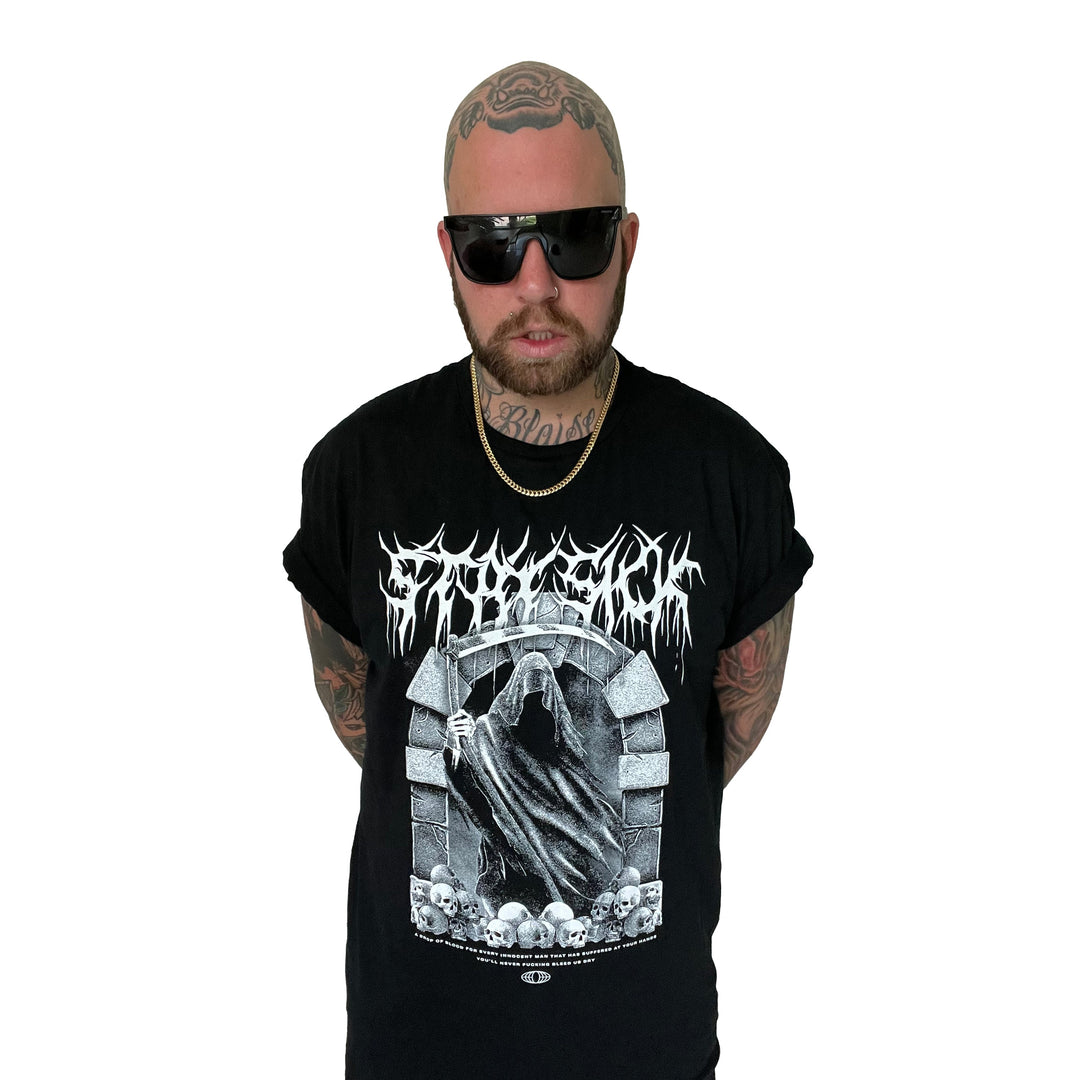 A bald, tattooed man with a beard and dark sunglasses wears a Stay Sick Clothing black T-shirt with a gothic Reaper skull design and a gold chain, standing against a plain white background.