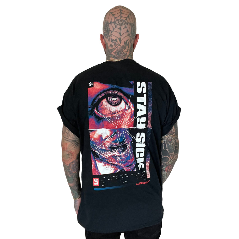 A tattooed person faces away, wearing the Stay Sick Clothing Legacy Black T-Shirt with a colorful eye and face graphic, and STAY SICK printed vertically on the back.
