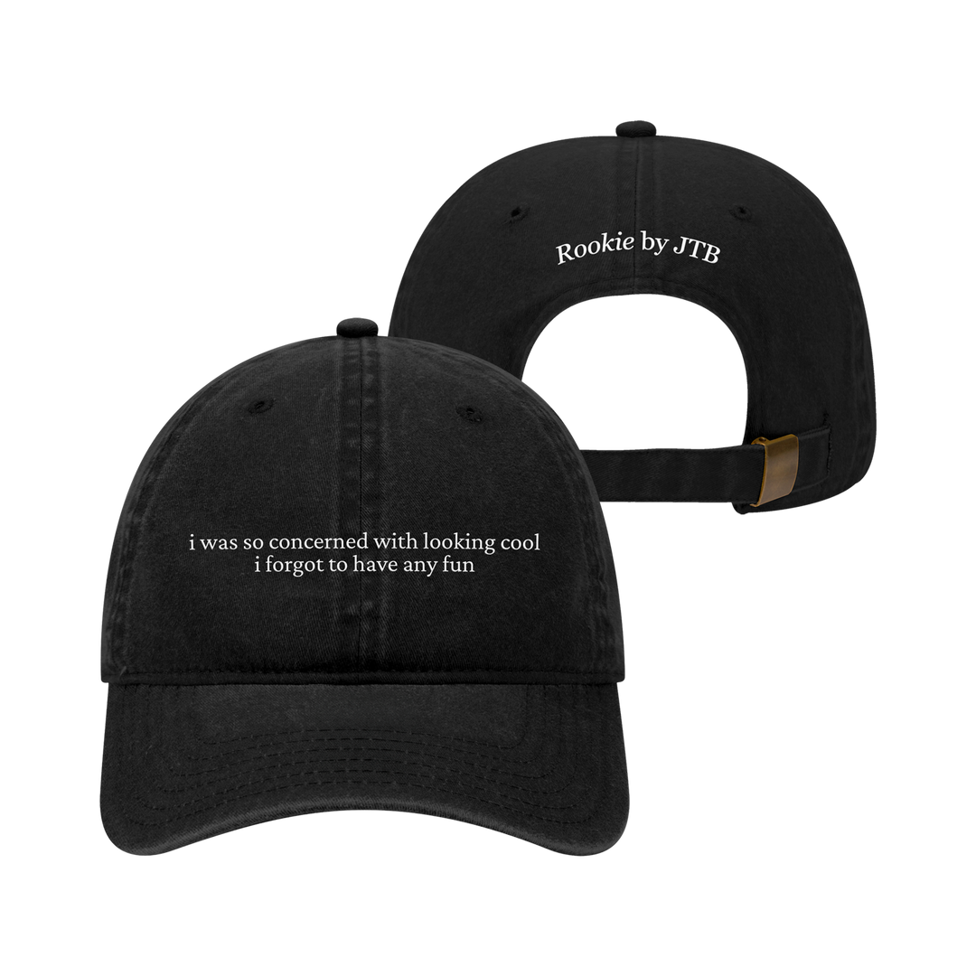 Two black Dad Hats from Joshua Bassett. The front features embroidered white text: "i was so concerned with looking cool i forgot to have any fun." Above the back strap, "Rookie by JTB" is stitched in white.