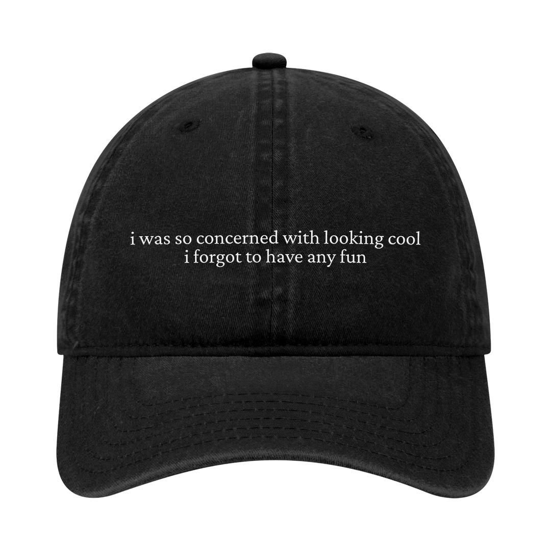 A black dad hat from Joshua Bassett, embroidered with white text on the front: i was so concerned with looking cool i forgot to have any fun.