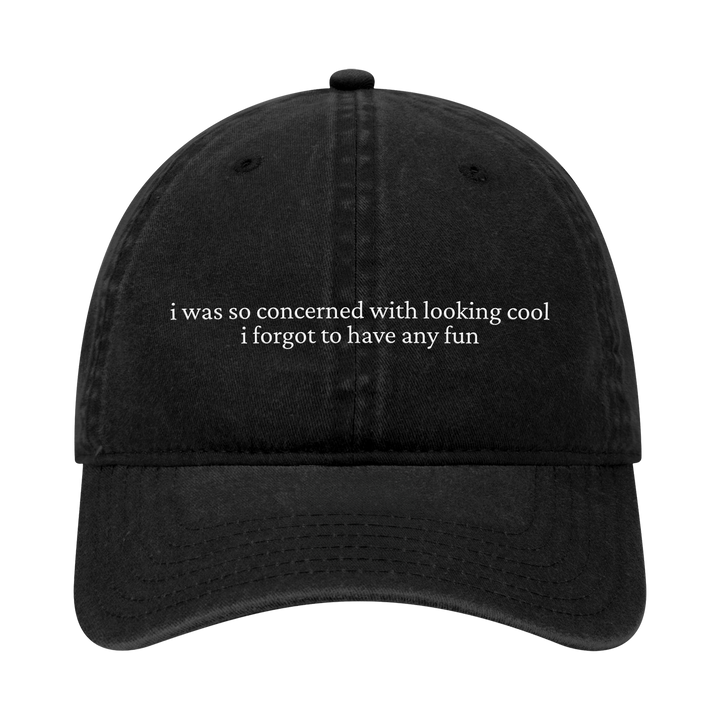 A black dad hat from Joshua Bassett, embroidered with white text on the front: i was so concerned with looking cool i forgot to have any fun.