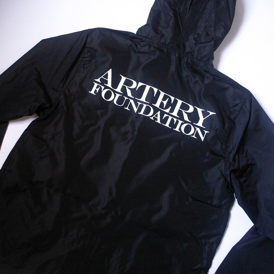 A black zip-up jacket from Artery Foundation laid flat, featuring large white capital letters spelling the brand name on the back.