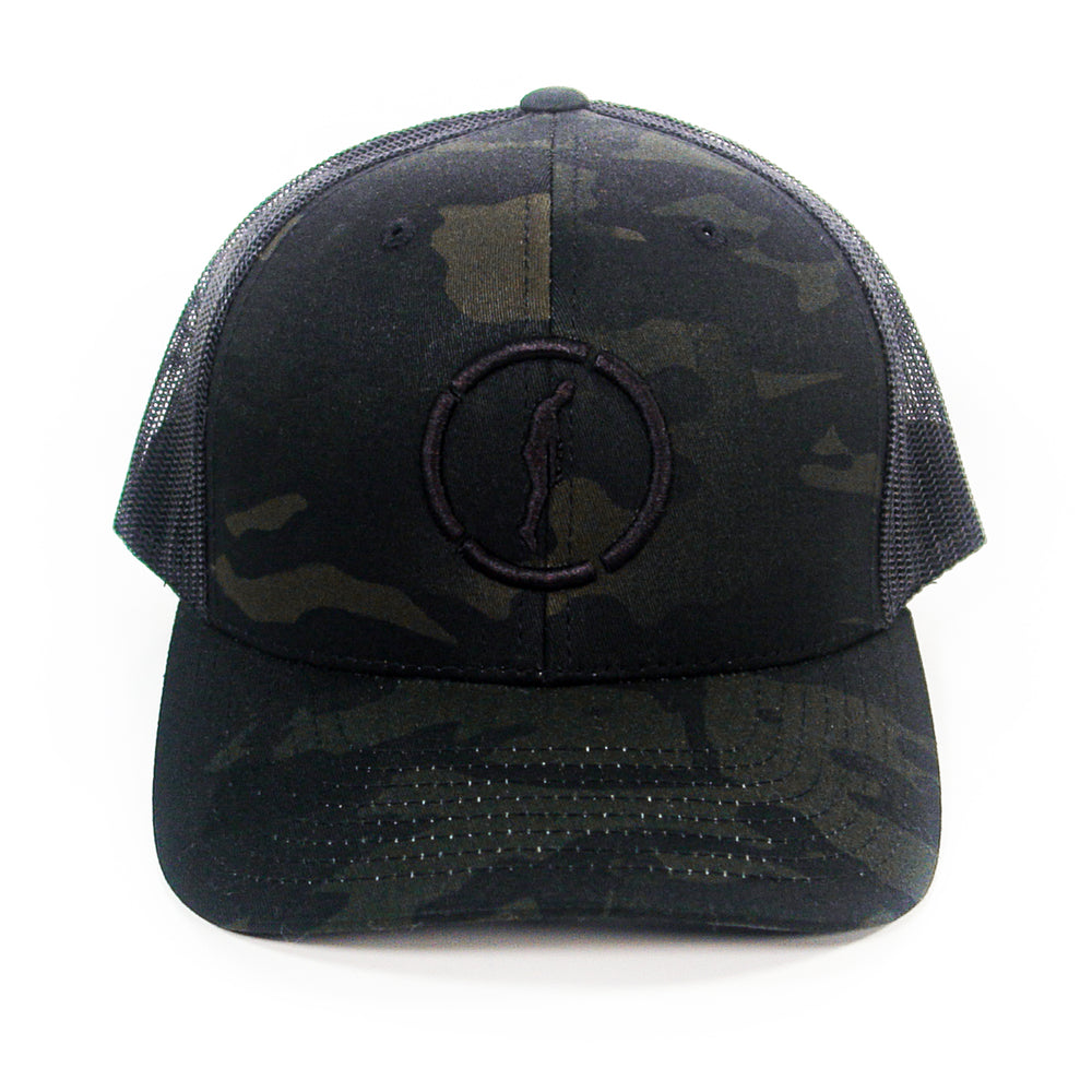 A black camouflage Hopesfall trucker hat with a mesh back and a subtle embroidered circle and figure logo on the front, displayed against a white background.