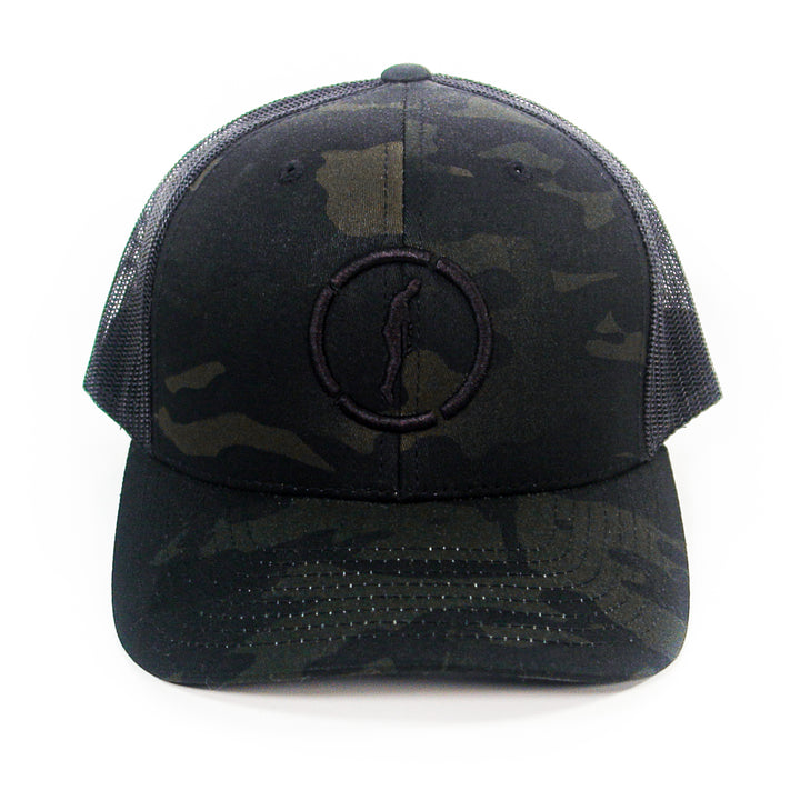 A black camouflage Hopesfall trucker hat with a mesh back and a subtle embroidered circle and figure logo on the front, displayed against a white background.