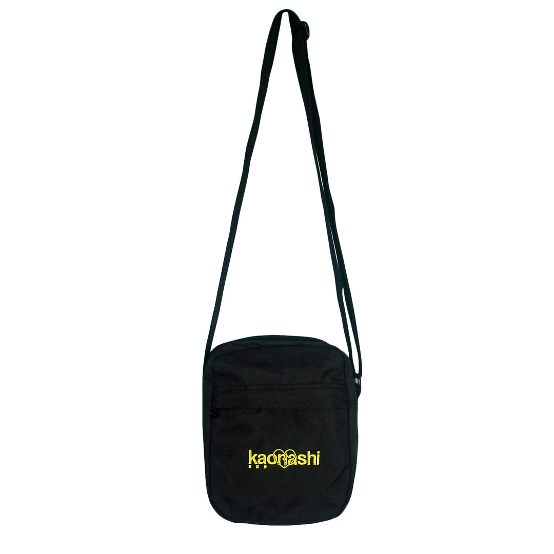 A black recycled polyester Kaonashi bag with a long adjustable strap, front zippered pocket, and "Kaonashi" embroidered in yellow—styled after AS Colour Flight Bags.