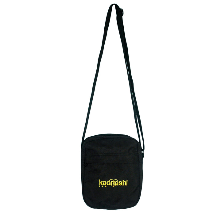 A black recycled polyester Kaonashi bag with a long adjustable strap, front zippered pocket, and "Kaonashi" embroidered in yellow—styled after AS Colour Flight Bags.