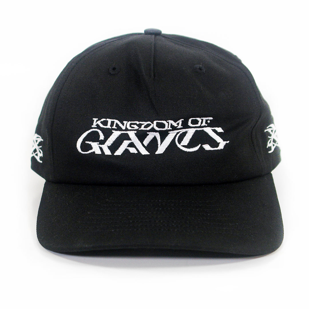 A black five-panel snapback hat from Kingdom Of Giants, featuring white embroidered text on the front that reads KINGDOM OF GRAVES. This adjustable cotton hat also has white embroidered symbols on both sides.