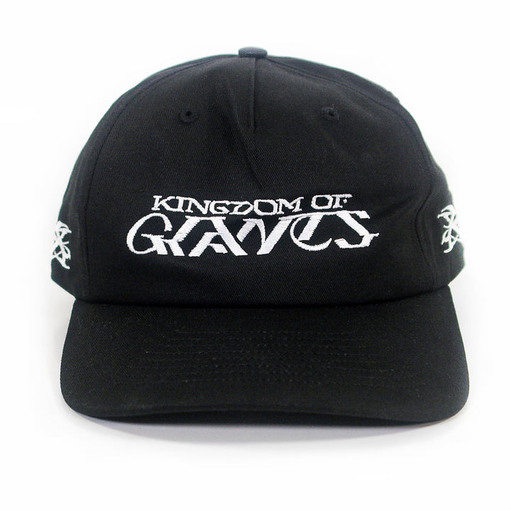 A black five-panel snapback hat from Kingdom Of Giants, featuring white embroidered text on the front that reads KINGDOM OF GRAVES. This adjustable cotton hat also has white embroidered symbols on both sides.