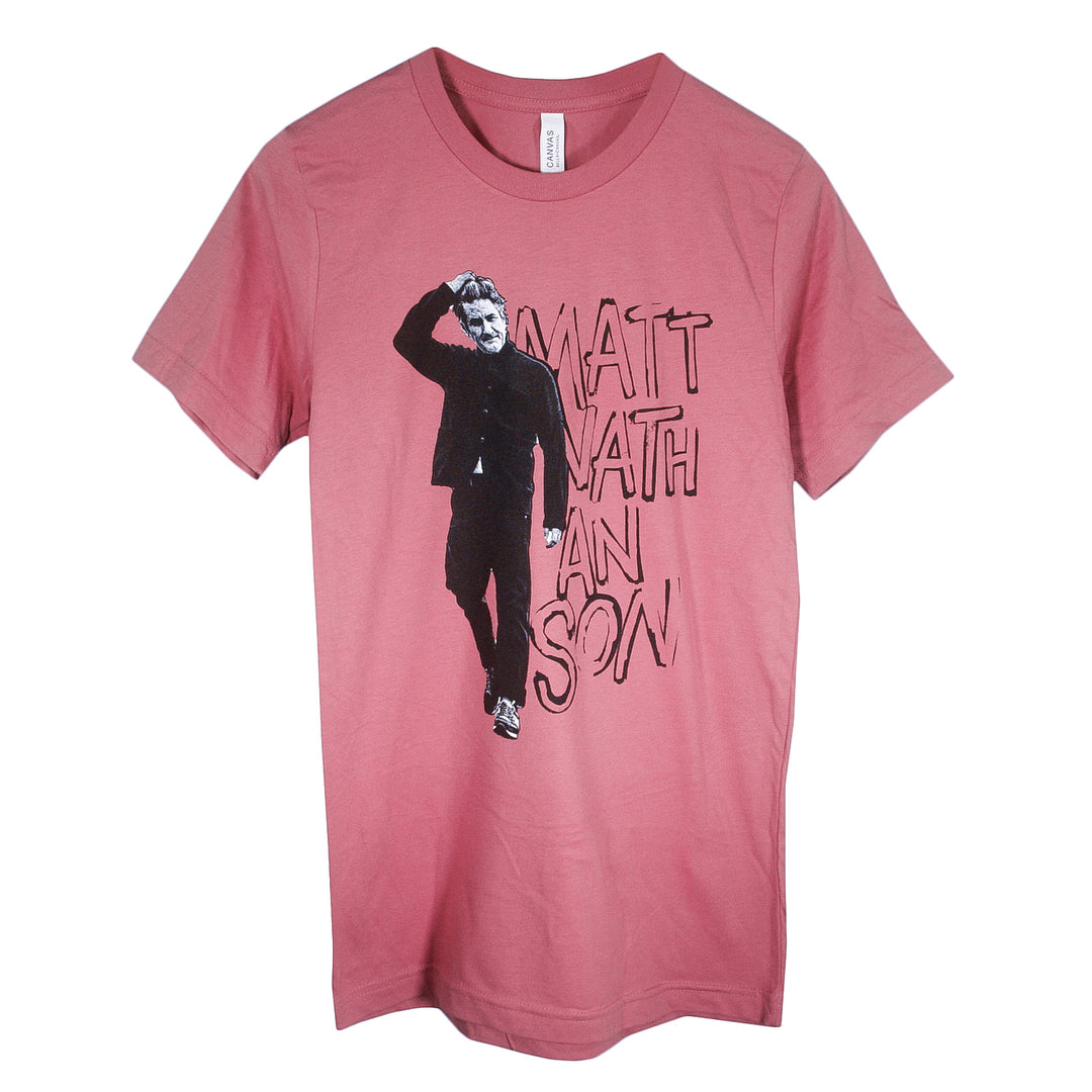 A pink Matt Nathanson T-shirt with a black-and-white graphic of a man walking and saluting, plus hand-drawn "MATT NATHANSON" text. Made from soft Airlume combed cotton and designed in unisex sizing for comfort.