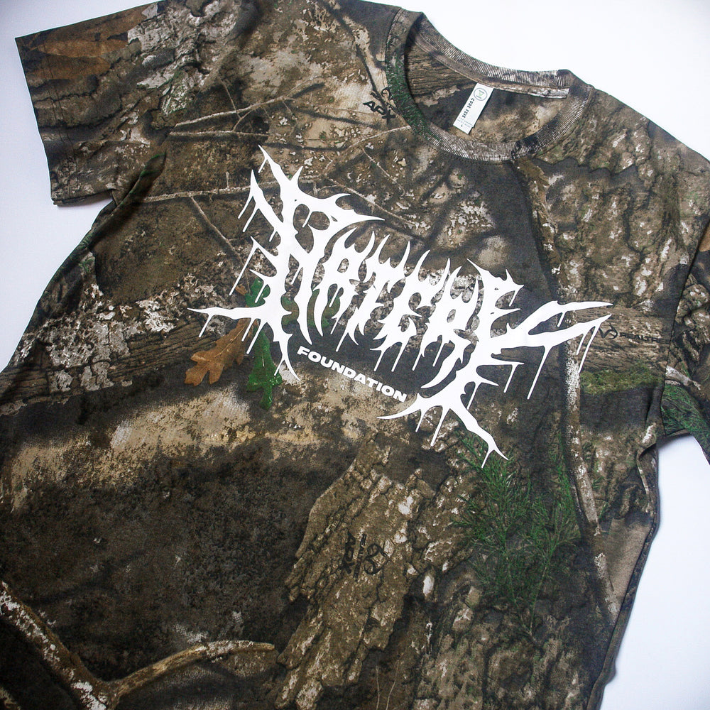 An Artery Foundation REALTREE camo t-shirt features "FOUNDATION" and an abstract white graphic across the chest. Made from soft ring-spun cotton, the shirt is shown laid flat on a white background.