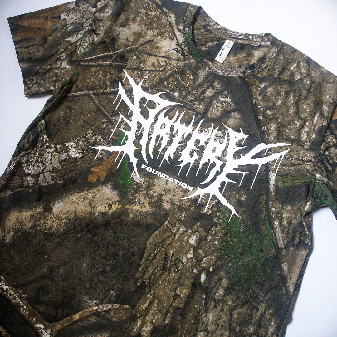 An Artery Foundation REALTREE camo t-shirt features "FOUNDATION" and an abstract white graphic across the chest. Made from soft ring-spun cotton, the shirt is shown laid flat on a white background.