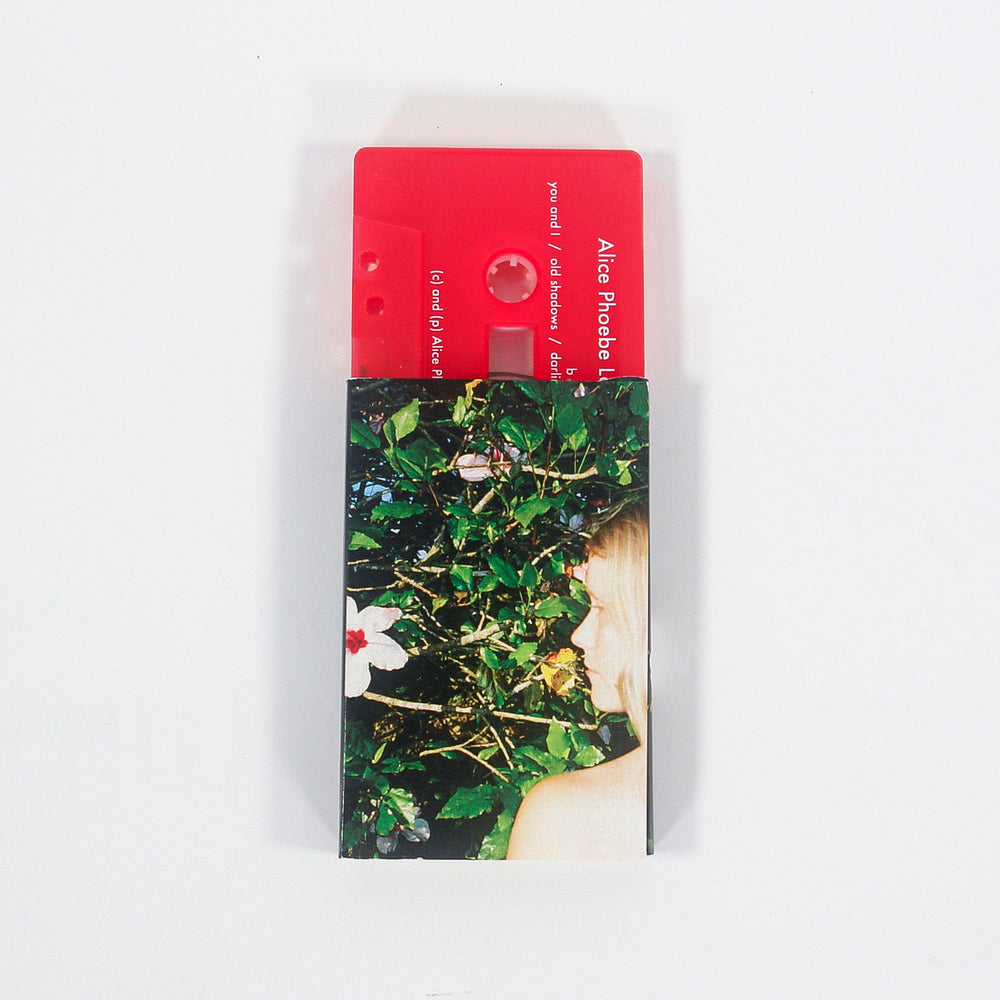 A red cassette tape labeled Alice Phoebe partially slides out of a sleeve featuring a woman with blonde hair standing in front of green foliage and blooming flowers, capturing a nostalgic music cassette vibe that hints at the dreamy mood of Oblivion.