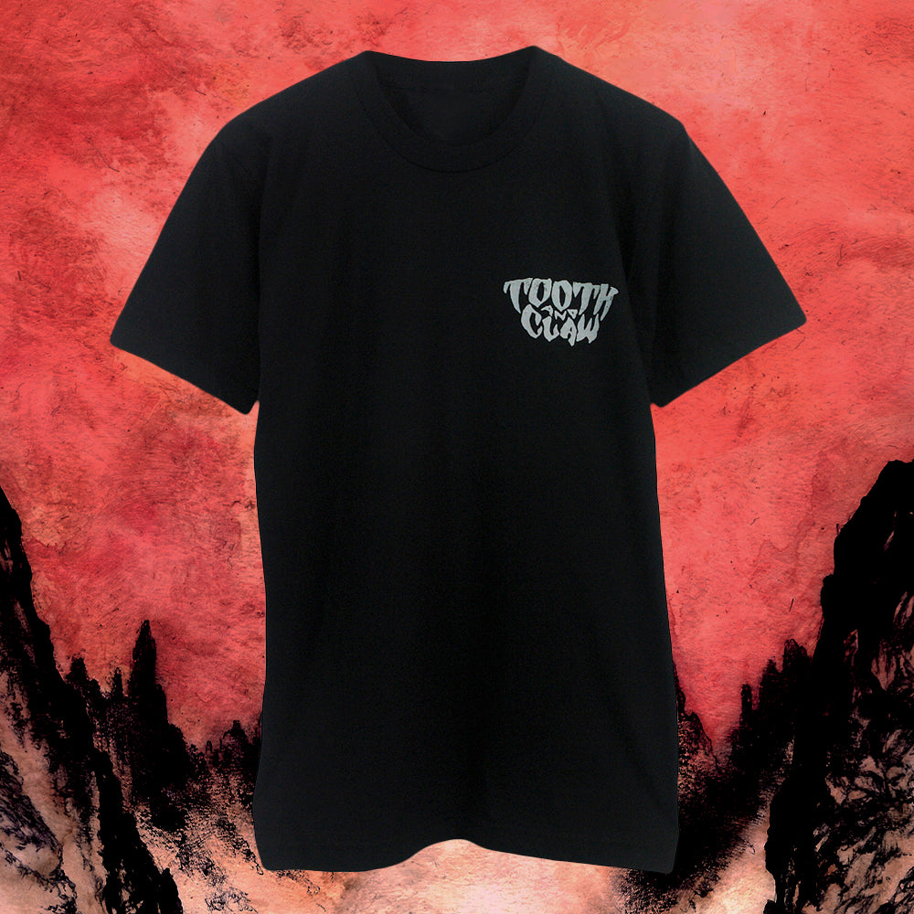 A black Tooth And Claw Next Level Apparel T-shirt with a small white "TOOTH CLOW" graphic on the left chest, made from soft ringspun cotton and displayed against a red and black rocky background.