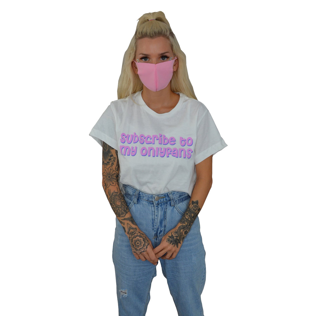 A blonde woman wearing a pink face mask and Stay Sick Clothing’s white cropped shirt with Subscribe to my onlyfans in purple stands with her hands together against a white background.