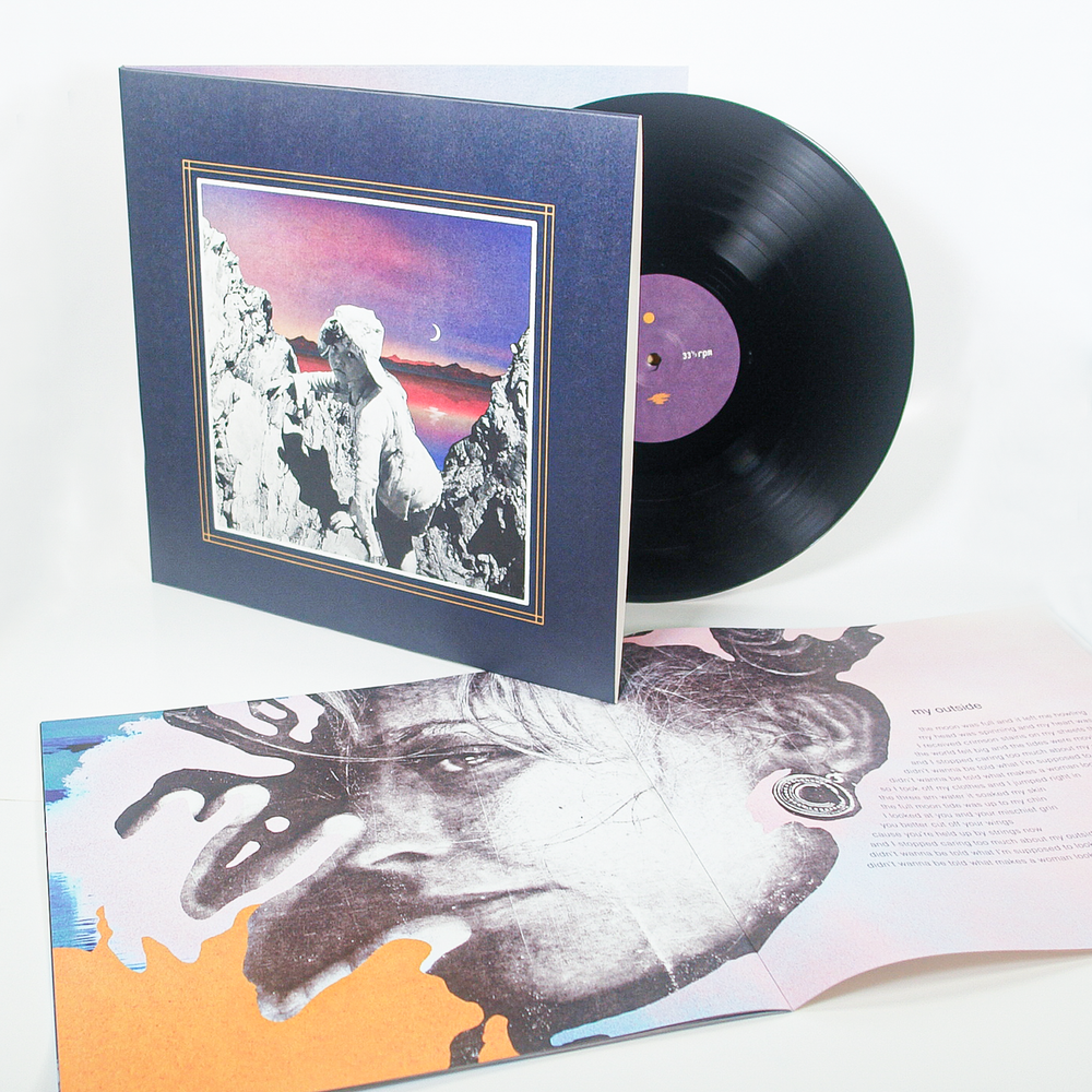 A vinyl record with a purple label is partly out of its square sleeve featuring a collage-style cover. An open booklet with a black-and-white face and text lies in front, showing an artistic, colorful design inspired by the dreamy theme of Galaxies and the whimsical tones of Little Spark.