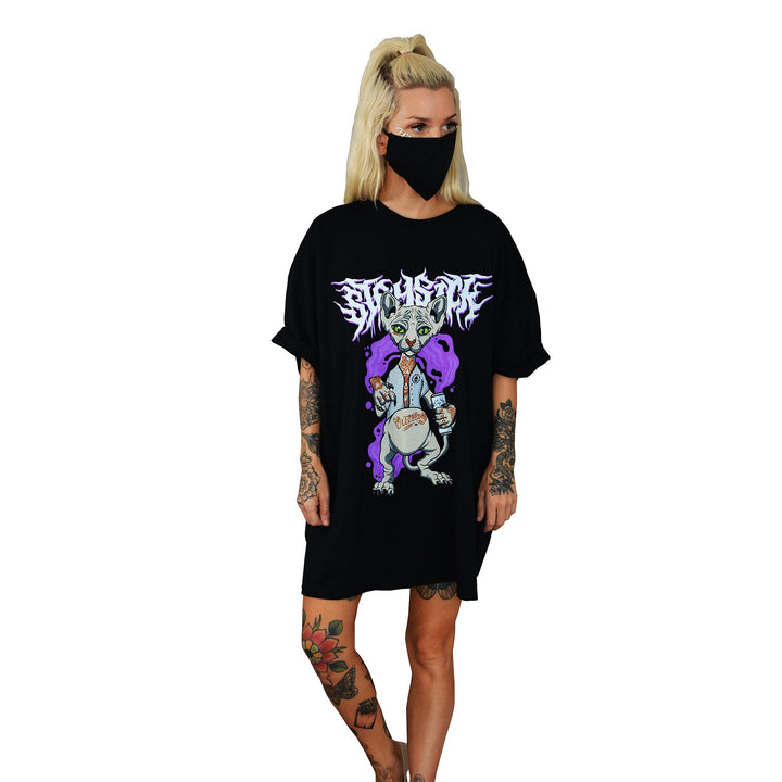 A blonde woman with a ponytail and tattoos sports a black face mask and an oversized Stay Sick Clothing Party Karl T-shirt with a cartoon vampire and bold white text, giving her partywear look an edgy vibe.