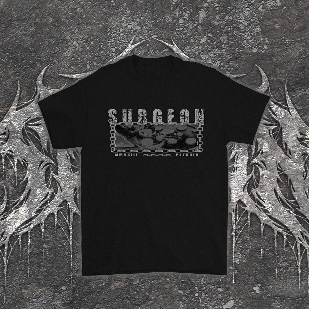 Black Petunia t-shirt featuring a rectangular graphic with the word SURGEON above metallic medical instruments framed by a chain, with MMXXIII printed below.
